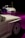 Two sleek white cars are showcased, positioned on a glossy purple floor. The foreground features a close-up of one car's side, highlighting its intricate wheel design. In the background, a second car is seen, adding depth to the scene with a dark ambient setting enhancing the vehicles.