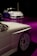 Two sleek white cars are showcased, positioned on a glossy purple floor. The foreground features a close-up of one car's side, highlighting its intricate wheel design. In the background, a second car is seen, adding depth to the scene with a dark ambient setting enhancing the vehicles.