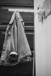 Stylish denim jacket hanging on a rustic wooden hanger against a brick wall.