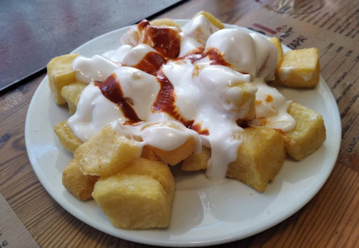 Close-up of a rustic wooden table with patatas bravas and alioli sauce.