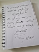 A spiral-bound notebook with handwritten text in dark ink. The writing expresses a message about embracing imperfections and acknowledges having many flaws. The handwriting is cursive and artistic, emphasizing the unique and personal nature of the note.