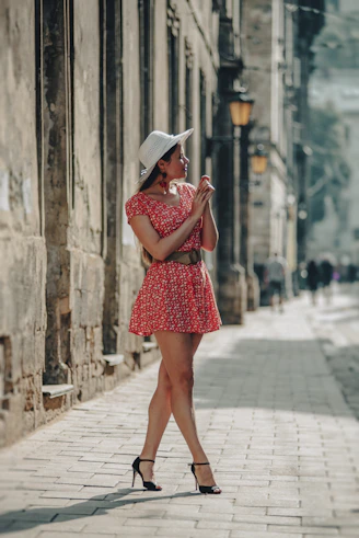 a woman in a red dress and hat walking down a street