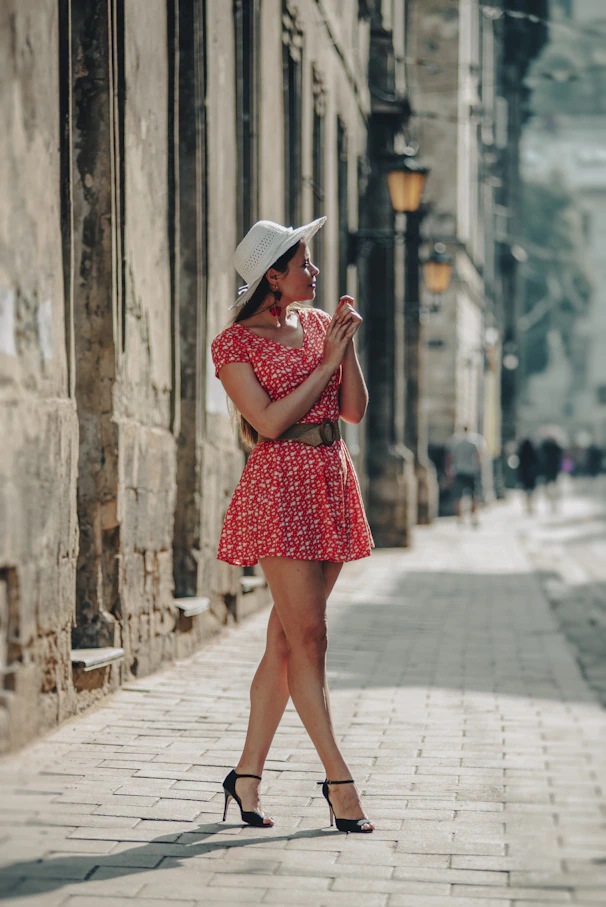 a woman in a red dress and hat walking down a street