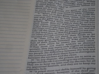 A close-up view of a page from a book, possibly a religious or sacred text, with columns of text printed in a serif font. The left side of the page features a column of dots, possibly indicating a section or chapter demarcation. The text is laid out in a structured format, suggesting guidelines or instructions.