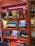 Shelves stocked with various brands of liquor, including bottles of whisky and gin. The display features brands like Dewar's, Monkey Shoulder, Jameson, Chivas, The Glenlivet, and others. The shelves are brightly colored with orange and red patterns.
