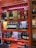 Shelves stocked with various brands of liquor, including bottles of whisky and gin. The display features brands like Dewar's, Monkey Shoulder, Jameson, Chivas, The Glenlivet, and others. The shelves are brightly colored with orange and red patterns.