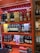 Shelves stocked with various brands of liquor, including bottles of whisky and gin. The display features brands like Dewar's, Monkey Shoulder, Jameson, Chivas, The Glenlivet, and others. The shelves are brightly colored with orange and red patterns.