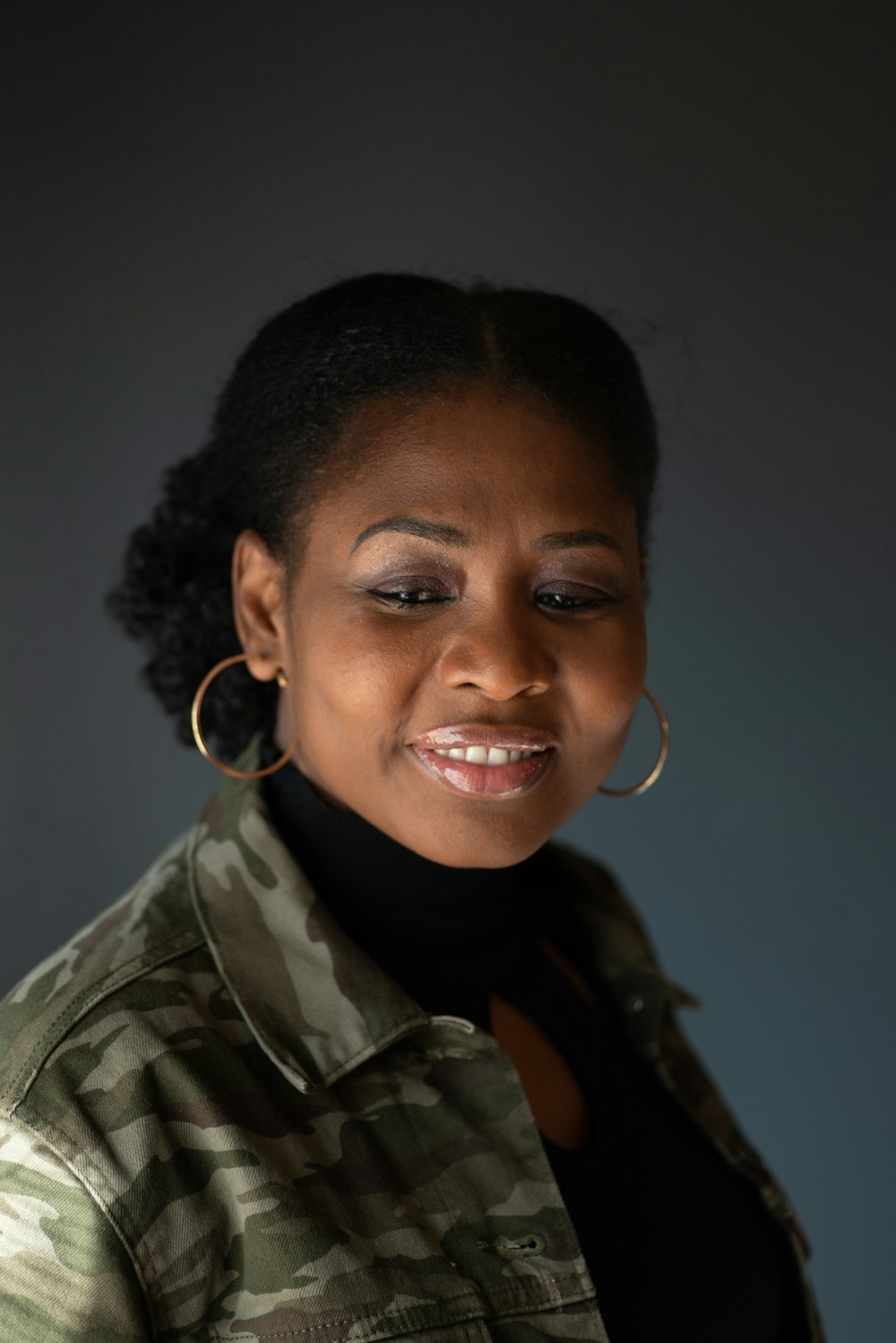 a woman in a camouflage jacket smiles at the camera