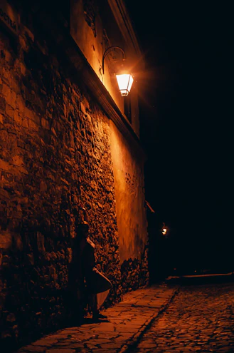A cobblestone street illuminated by warm street lamps, with a classic film camera set up capturing the moment.