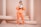 A person in an orange outfit is holding a soccer ball and wearing sunglasses, standing in front of a background adorned with architectural columns. The setting has a minimalistic design and a monochromatic color scheme.