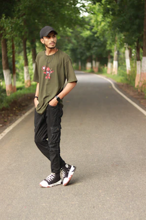 Young man wearing olive green streetwear t-shirt standing against a textured urban wall.