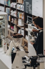 Barista carefully pouring latte art into a cup with a backdrop of coffee bags.