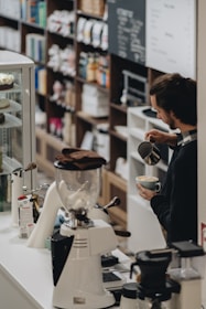 Barista carefully pouring latte art into a cup with a backdrop of coffee bags.