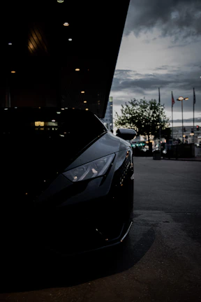 Side profile of a black luxury car featuring tinted windows reflecting a cityscape at dusk with red highlights.