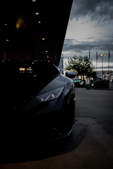 Close-up of a sleek black sports car hood reflecting ambient city lights at dusk.