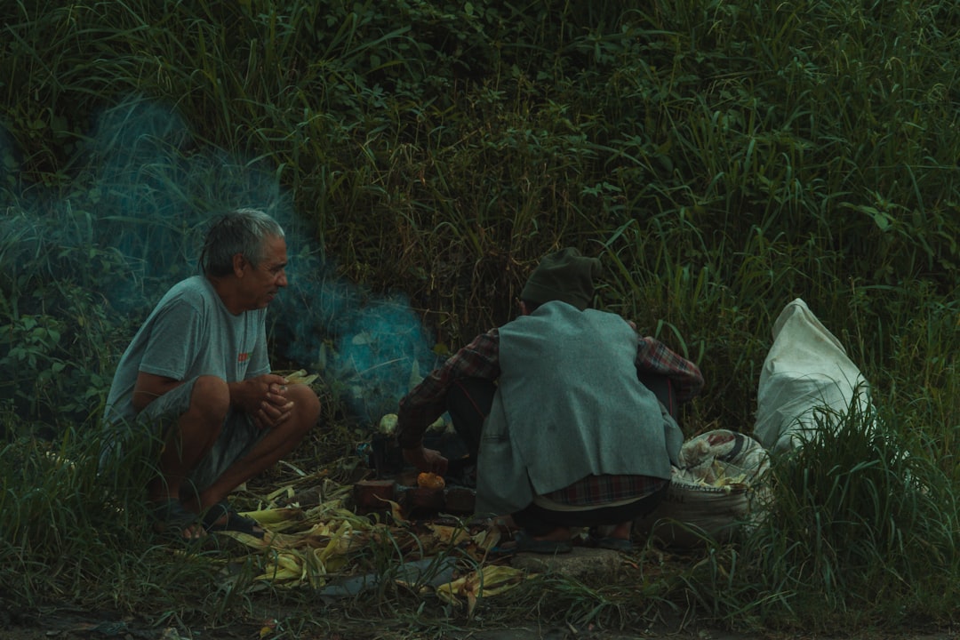 a man and a woman sitting on the ground next to a forest,