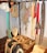 A collection of traditional harness equipment, including ropes, harness pads, and leather straps, hangs on a wall. There are several coils of rope and various colored straps. Wooden and leather saddles are placed on the floor, alongside wooden boxes with tools and accessories.
