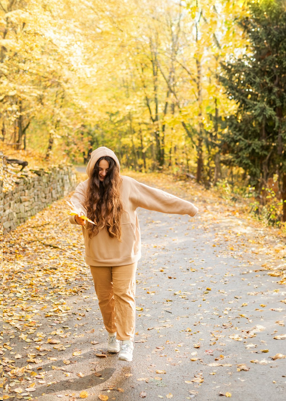 a woman walking down a leaf covered road