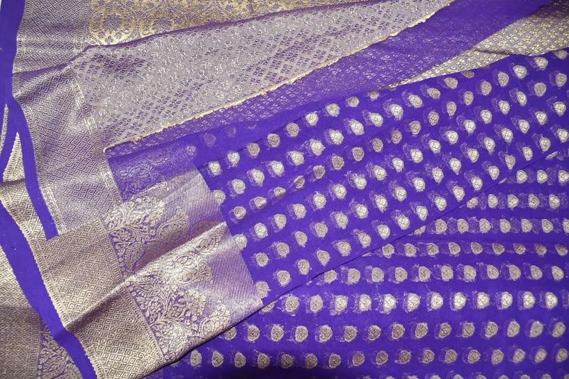 A richly patterned fabric with intricate silver detailing and a vibrant purple background. The design features floral and geometric motifs, giving it a luxurious and traditional appearance.