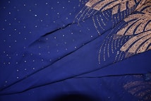 A fabric with a deep blue background is adorned with intricate gold patterns and small sparkling dots. The patterns resemble fireworks or radial designs, creating an elegant and luxurious look.