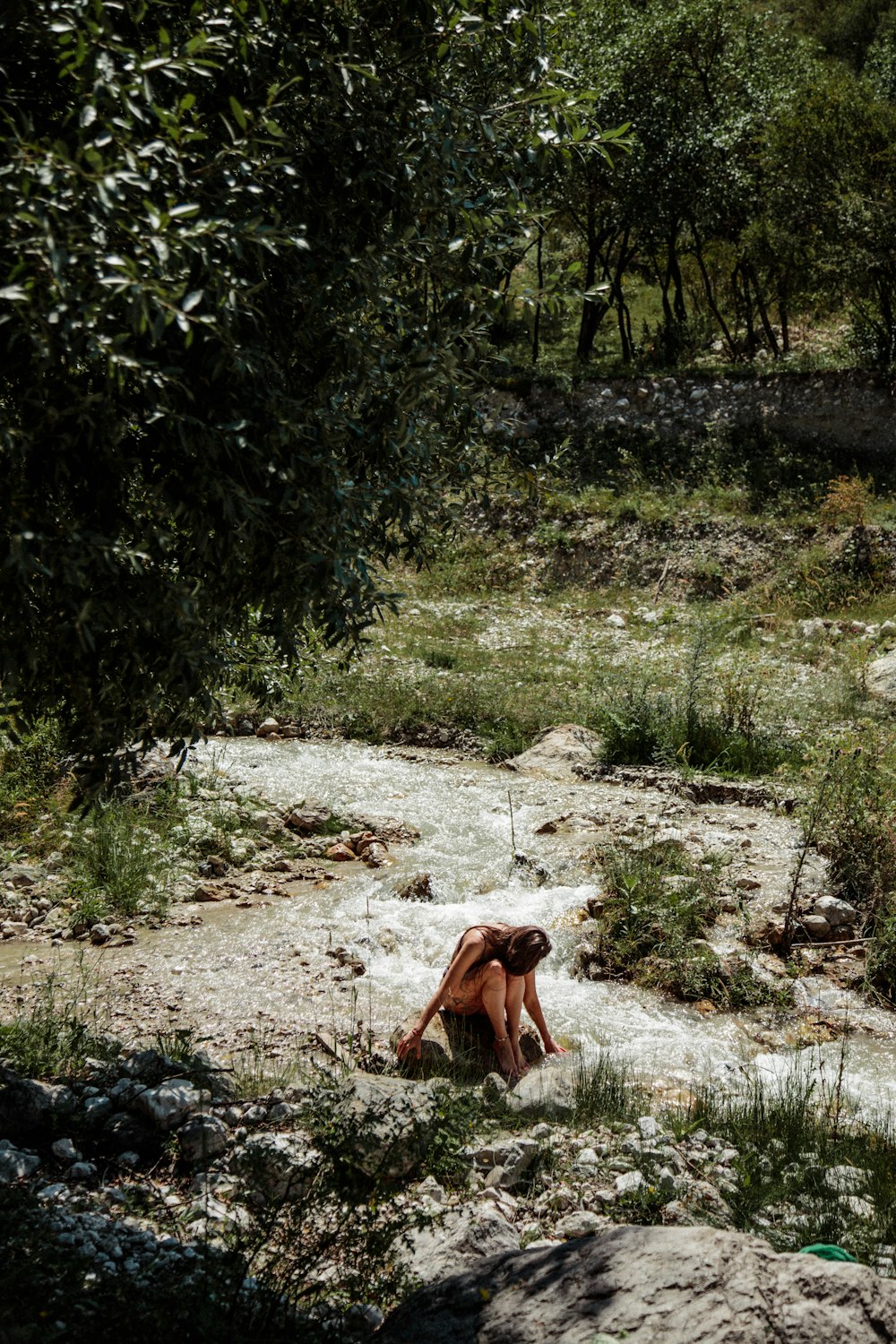a woman sitting on the ground next to a river