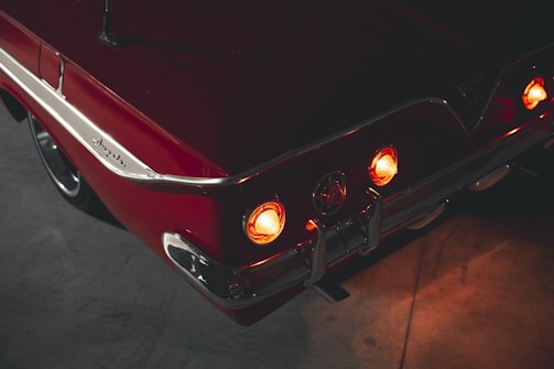 A gleaming vintage muscle car with a glossy cherry red paint job parked under soft evening lights.