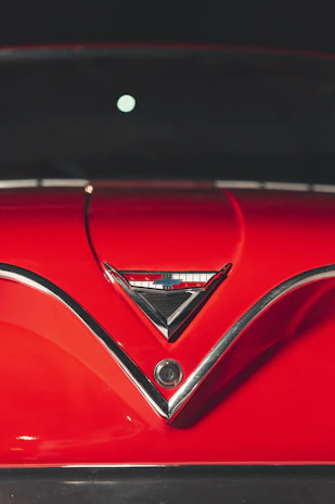 Close-up of a shiny restored classic car hood with Automack’s logo reflected on the surface.