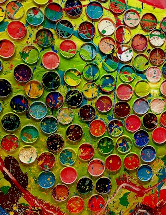 Hands painting a vibrant abstract design, surrounded by scattered paint tubes.