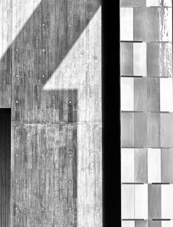 Black and white close-up of a raw concrete facade with sharp geometric shadows.