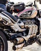 A close-up view of a powerful motorcycle featuring a sleek design with metallic and black components. The engine and exhaust system are prominently displayed, and a small bag is attached on top. The motorcycle tank displays a Union Jack design.