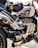 A close-up view of a powerful motorcycle featuring a sleek design with metallic and black components. The engine and exhaust system are prominently displayed, and a small bag is attached on top. The motorcycle tank displays a Union Jack design.