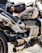 A close-up view of a powerful motorcycle featuring a sleek design with metallic and black components. The engine and exhaust system are prominently displayed, and a small bag is attached on top. The motorcycle tank displays a Union Jack design.