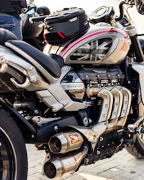 A close-up view of a powerful motorcycle featuring a sleek design with metallic and black components. The engine and exhaust system are prominently displayed, and a small bag is attached on top. The motorcycle tank displays a Union Jack design.