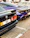 Two luxury cars, a black BMW M3 and a blue McLaren, are parked side by side on a paved parking lot. Both vehicles feature sleek, sporty designs, and the image captures their rear ends. The number plates are visible, showing a Dubai registration.