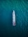 An overhead view of a large ship navigating through a vast expanse of deep blue ocean. The ship is centrally positioned, showcasing its streamlined design and various components visible on deck, including lifeboats and equipment.
