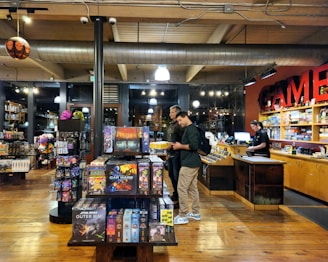 Cozy store corner filled with shelves of board games, trading cards, and video games with friendly staff assisting customers.