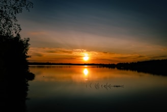 A serene sunset over a still lake, with soft ripples reflecting the golden light.