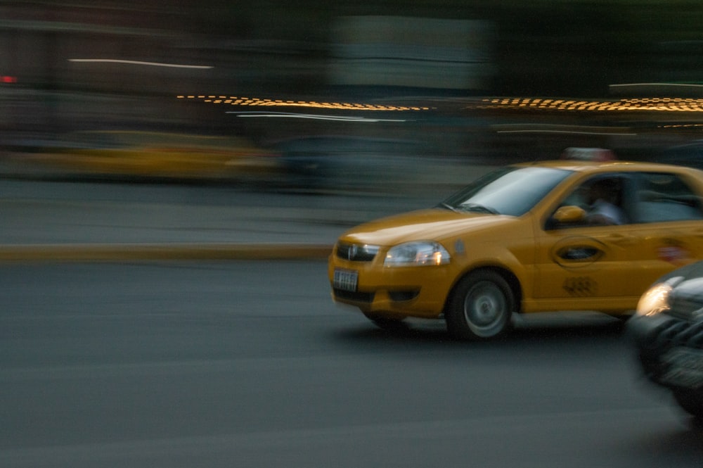 a yellow taxi driving down a street next to a motorcycle
