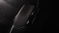 A close-up view of a black computer mouse with a textured scroll wheel. The surface appears matte with subtle reflections under dim lighting, highlighting its sleek design.