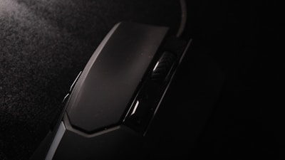 A close-up view of a black computer mouse with a textured scroll wheel. The surface appears matte with subtle reflections under dim lighting, highlighting its sleek design.