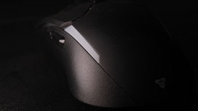 A modern, sleek computer mouse sits on a dark surface. The mouse has a matte finish with a subtle logo on the side. The lighting highlights the contours and enhances the elegant design.