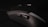 A close-up view of a black gaming mouse with multiple buttons and a textured surface, set against a dark background. The focus is on the side buttons, highlighting the ergonomic design of the device.