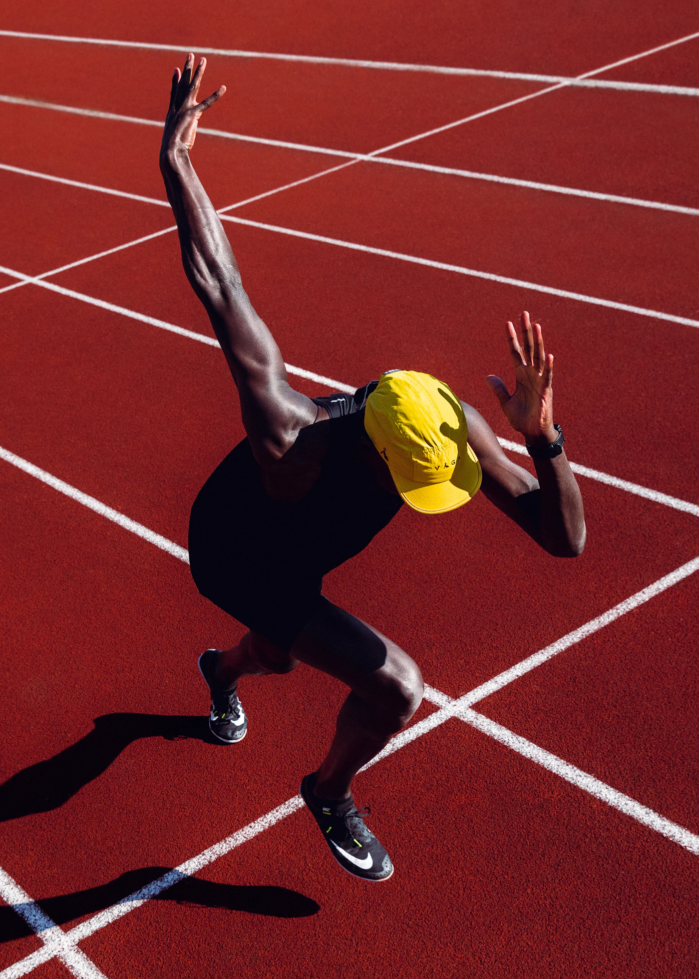 Mock photo: a Black sprinter in a yellow cap exploding off the line on a red track. Replaced by store photography from the shoot.