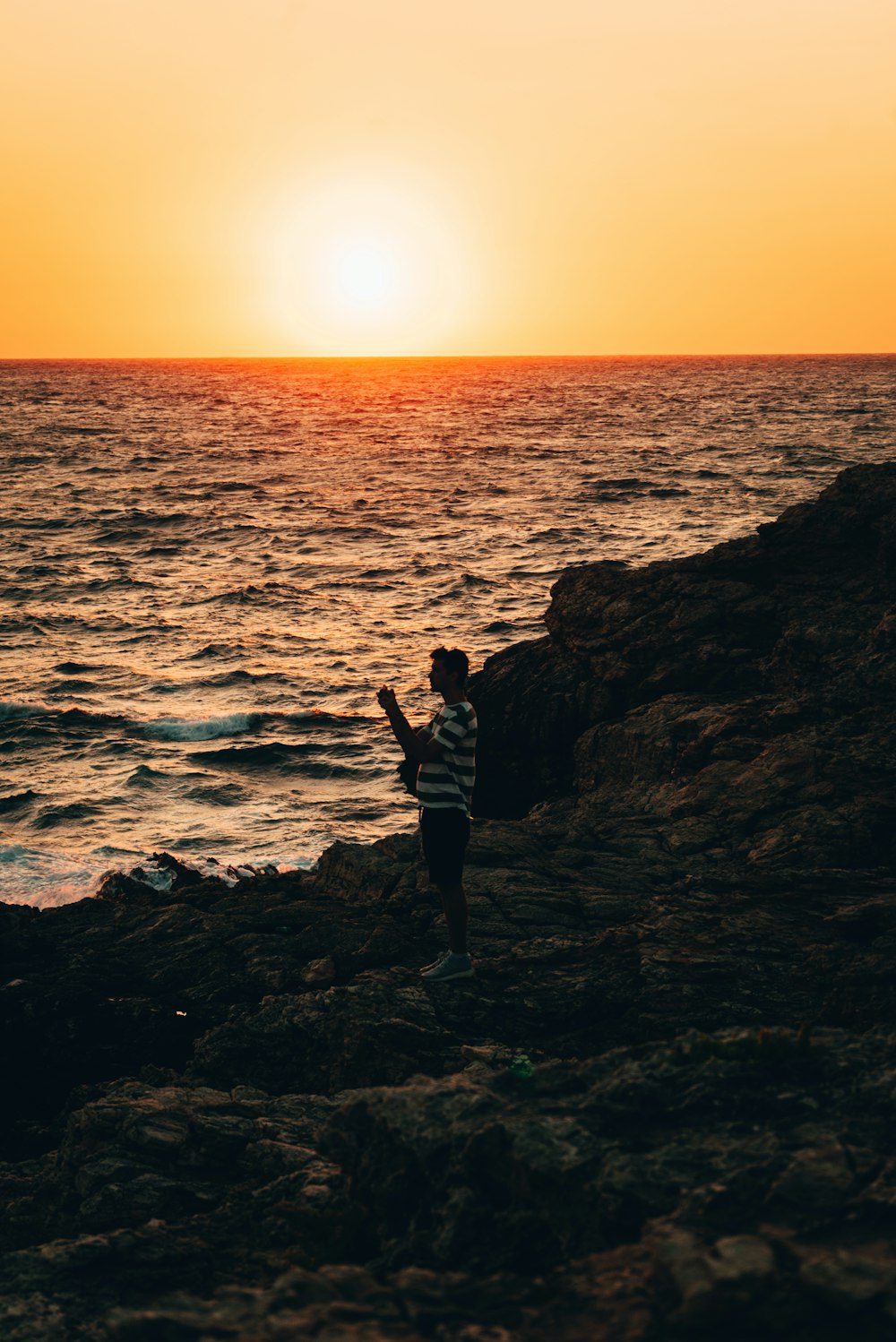 a man standing on top of a rocky beach next to the ocean