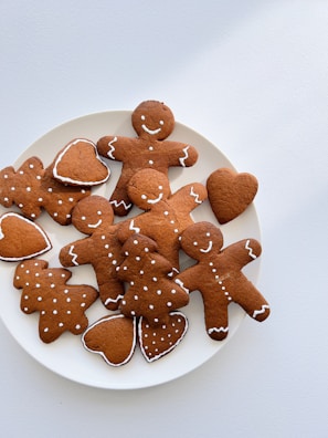 A plate filled with gingerbread cookies in various shapes, including gingerbread men, trees, and hearts, all decorated with white icing details.