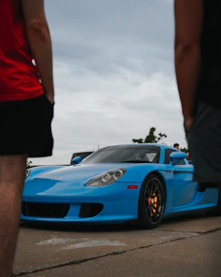A sleek car parked in a driveway with a smiling couple admiring it.