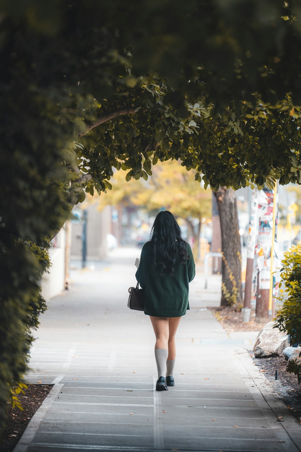 a woman walking down a sidewalk under a tree