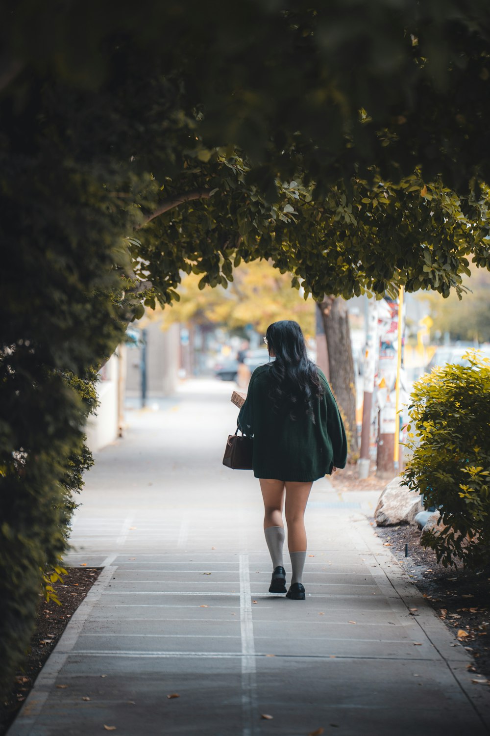 a woman walking down a sidewalk under a tree