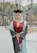 A smiling young male student in graduation gown holding a medical textbook, standing in front of a university campus.