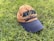 A baseball cap with the words 'Abu Dhabi' and 'United Arab Emirates' embroidered on it rests on a patch of lush green grass. The cap is two-toned, with a tan crown and a navy blue brim.